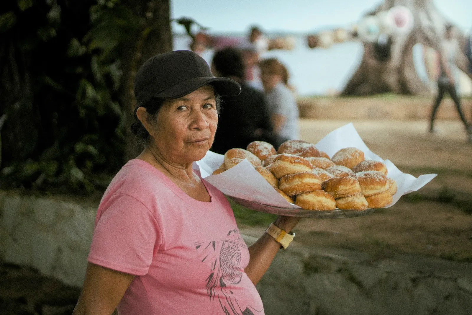 Vendedora ambulante segurando uma bandeja de rosquinhas na praia