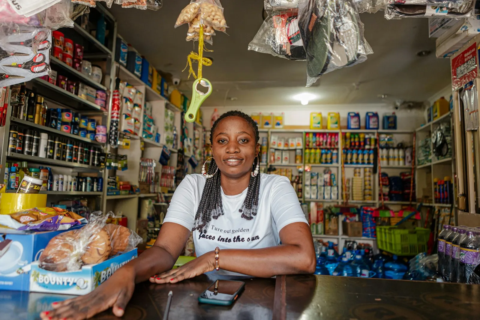 Lojista atrás do balcão de um mercadinho de bairro, com prateleiras de produtos ao fundo